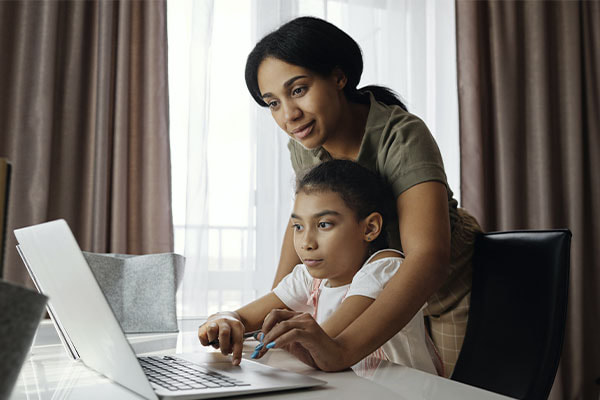 Photo of a mother helping her daughter do her homework on the computer. This represents how neuropsychological evaluations in Texas can help children experiencing academic or behavioral challenges.